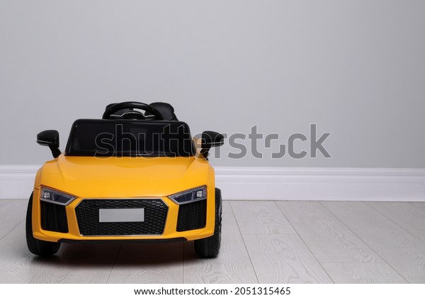 Child\'s electric toy car near light wall indoors.\
Space for text