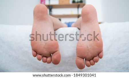 The child's feet hanging from the bed. The child is lying on the bed. Healthy feet, no signs of flat feet