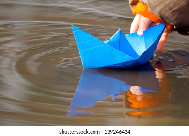 Child's Hand And Blue Paper Boat In Water In Spring
