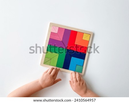 childs hand collects multicolored wooden mosaic on white background.