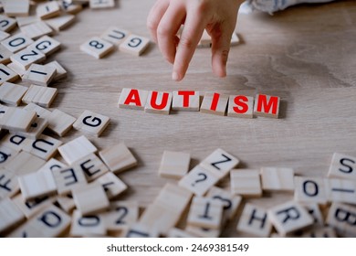 child's hand complete word "AUTISM," symbolizing importance of early diagnosis and intervention for children with autism, self-acceptance and embracing neurodiversity - Powered by Shutterstock