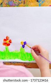 Child's Hand Drawing Flowers On White Sheet Of Paper On An Easel. Children's And Earth Day Concept.