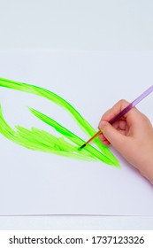 Child's Hand Drawing Green Leaf By Watercolors On White Sheet Of Paper. Earth Day Concept. Top View.