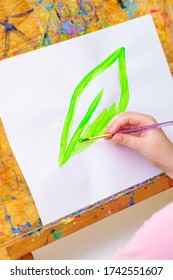 Child's Hand Drawing Green Leaf By Watercolors On White Sheet Of Paper On An Easel. Earth Day Concept.