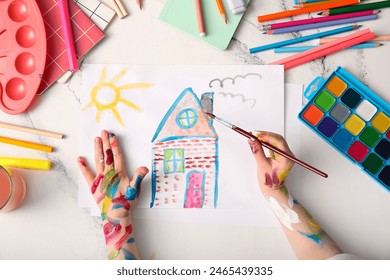 Child's hand drawing home with brush, watercolor paints and different stationery on white background - Powered by Shutterstock