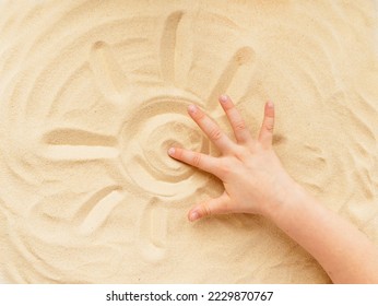 a childs hand draws the sun on the sand - Powered by Shutterstock