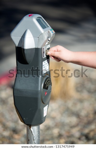 Child\'s hand feeding quarters to a parking meter for\
extra time