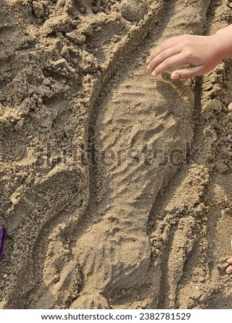 A child's hand gently touches a sand sculpture on the beach, revealing intricate patterns and textures amid the surrounding grains.