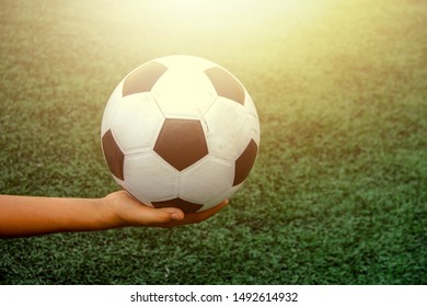 The Child's Hand Is Holding An Old Black And White Soccer Ball