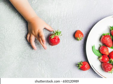 Child's hand holding strawberry on rustic concrete background, plate of strawberries. Summer healthy eating concept. Top view, flat lay. - Powered by Shutterstock