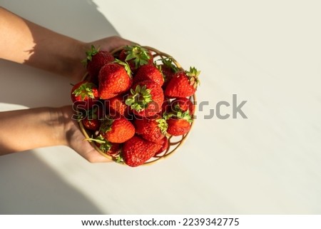Child's hand holding strawberry on rustic concrete background, plate of strawberries. Summer healthy eating concept
