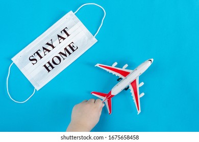 A Child's Hand Holds A Toy Airplane, Next To A Medical Mask With The Inscription Stay At Home. Evacuation Of People From Areas Infected With Coronavirus.