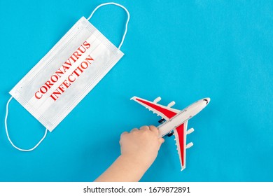 A Child's Hand Holds A Toy Airplane, Next To A Medical Mask With The Inscription Coronavirus Infection. Evacuation Of People From Areas Infected With Coronavirus.