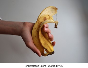 A child's hand with light skin holding a yellow banana peel with a few brown spots. Neutral background.
