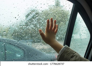 Child's Hand On The Window Pane Of The Car In The Raindrops.