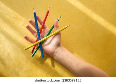 A child's hand pickina child's hand picking up coloured pencils on a yellow background . high quality photo - Powered by Shutterstock