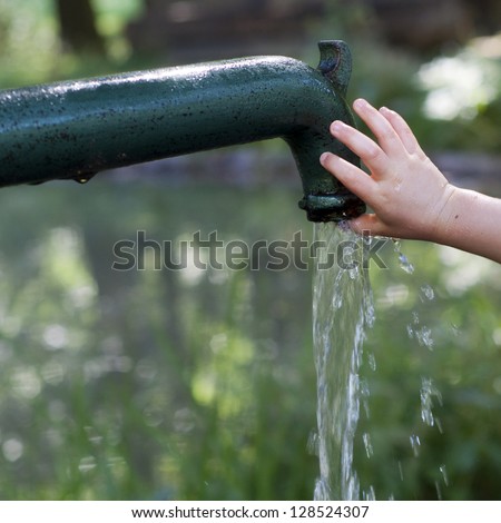 Child's hand playing with drinking water running  from an old  water pump; aid concept. .