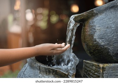 a child's hand playing a small artificial waterfall in the garden with morning light - Powered by Shutterstock