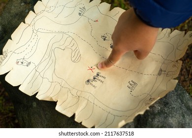 A child's hand points to the place where the treasures are buried. Active games for children. In search of a pirate treasure. Treasure map.
