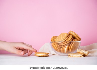 The child's hand takes a cookie from a glass bowl on a pink background. The concept of breakfast and a quick snack.