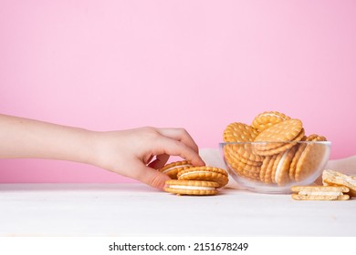 The child's hand takes a cookie from a glass bowl on a pink background. The concept of breakfast and a quick snack.