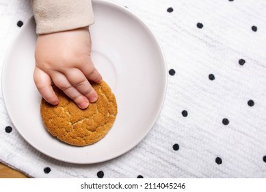 A child's hand takes a cookie from a plate. A white plate with cookies.