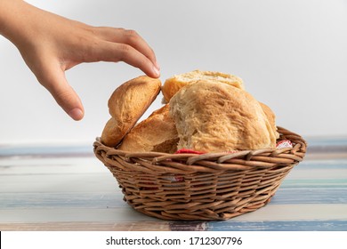 A child's hand taking a freshly baked loaf of bread from a basket on a colored wooden background. The concept of baking bread, eating meals with muffins, bread.