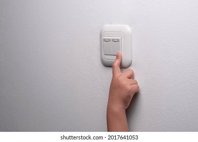 Child's Hand Turning Off A Light Switch Or Electrical Control On The Wall