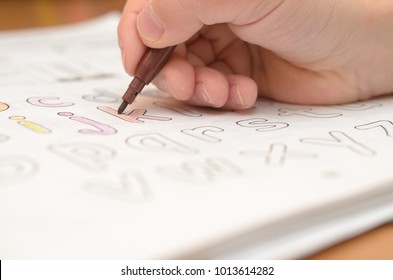 A child's hand writes and displays English letters in a notebook and alphabet with a pencil and felt-tip pen