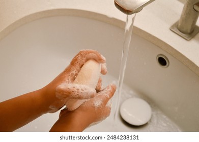 A child's hands are being washed with soap under a running tap, emphasizing the importance of hygiene. This image highlights the practice of proper hand washing for children. - Powered by Shutterstock