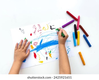 Childs hands drawing with colorful wax crayons on white paper, top view. Creative art concept for educational and developmental activities.
