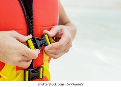 Child's Hands Fasten Life Jacket. Blurred Water In Background. Safety, Reliability Concept. Text Space.