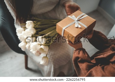 The child's hands hold a beautiful gift box with a ribbon and white tulips. Top view, close-up. Happy mother's day.