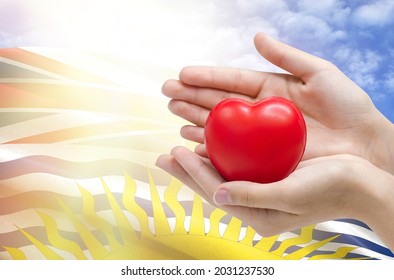 Child's hands hold a heart on the background of the flag of British Columbia, health care concept.