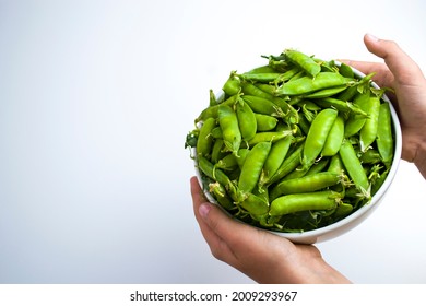 The child's hands hold a white cup full of pea pods, the daily norm of legumes for children.
