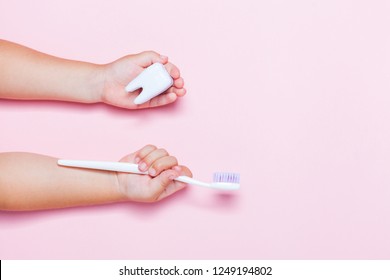 Child's hands holding big tooth and toothbrush on pink backgroubd. Healty care teeth concept. Top view, flat lay. Copy space for your text.