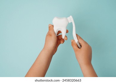 Child's hands holding white tooth and toothbrush on blue background. Healthy care teeth concept - Powered by Shutterstock