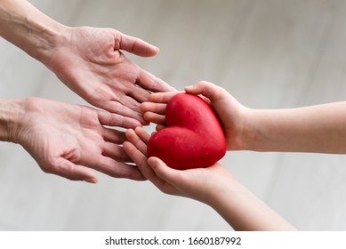 Childs Hands And Older Woman Hands Holding Heart. Concept O Love, Share And Care. Care For Elderly Concept.