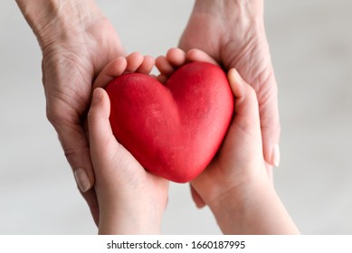 Childs Hands And Older Woman Hands Holding Heart. Concept O Love, Share And Care. Care For Elderly Concept.