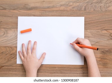 Child's hands and orange felt  tip the wooden table and piece paper  Top view 