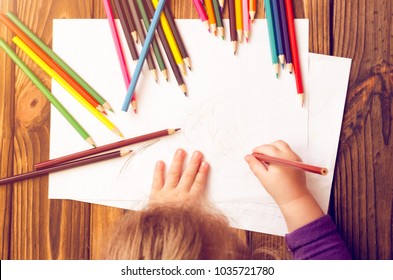 The child's hands are painted with colored pencils on a white sheet of paper on a wooden table. - Powered by Shutterstock