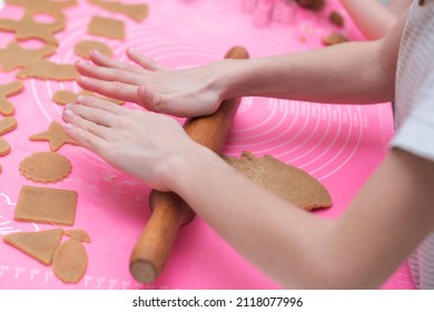 Child's hands roll dough for gingerbread with a rolling pin on a pink background. Close-up