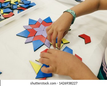 A child's hands are shown placing small, colorful, wooden shapes to form a larger tesselation on a white background. - Shutterstock ID 1426938227