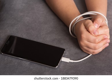 The Child's Hands Are Tied With A White Cord Of A Mobile Phone. Child's Dependence On Gadgets. The Social Problem Of Society. The Right Upbringing Of Children