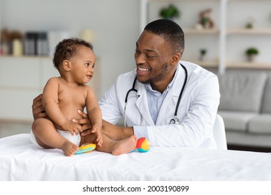 Child's Healthcare Concept. Portrait Of Smiling Black Doctor Making Check Up For Little Infant Baby Boy, Cute Toddler Child In Diaper Having Appointment At Pediatrician's Office, Free Space