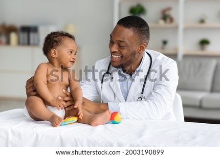 Child's Healthcare Concept. Portrait Of Smiling Black Doctor Making Check Up For Little Infant Baby Boy, Cute Toddler Child In Diaper Having Appointment At Pediatrician's Office, Free Space