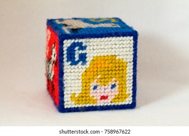 Child's Needlepoint Alphabet Block With Letter G And Image Of A Girl's Face. White Background.