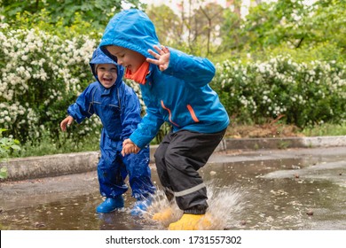 Childs in rainy day. Cute happy kids boys is jumping in the puddle. Bright spring rainy day. Kid in yellow rubber boots and rain suit, raincoat. Brothers outdoors.
