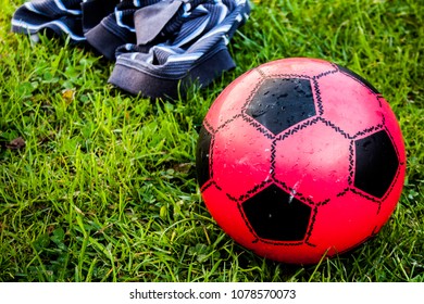 Child's Small Red Football On Green Grass With A  Jumper As A Goal Post