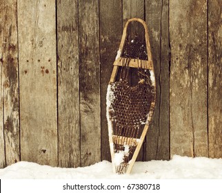 Child's Snow Shoe Standing Outside In The Snow Against A Rustic Wooden Barn Wall  With Copy Space.